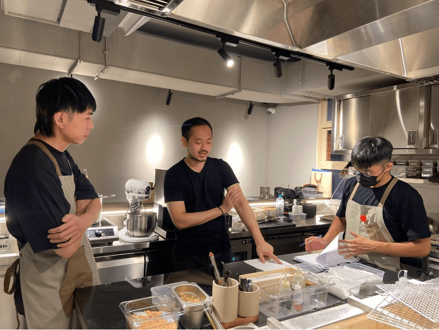 「直火1954」主廚陳柏翰（左）與時藝集團行政主廚蔡昀諺（中）和內場團隊工作討論。